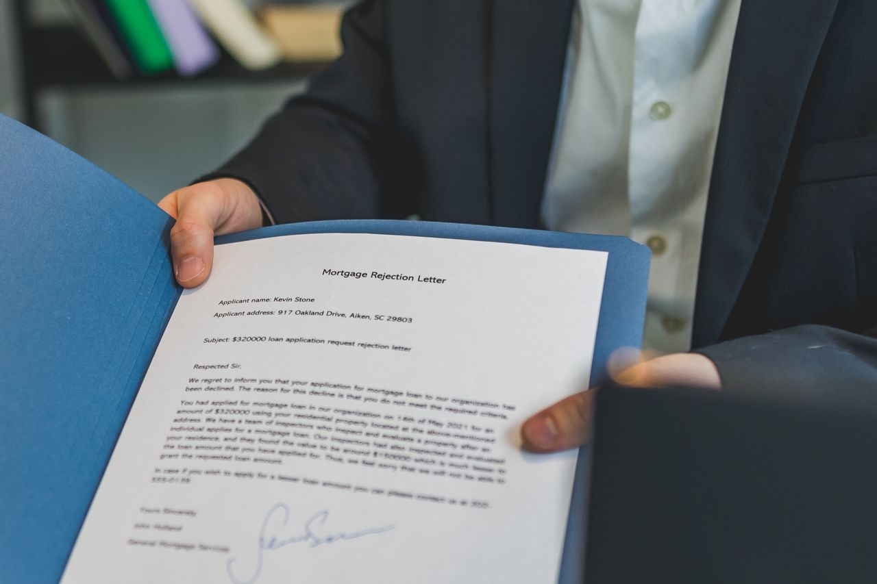 About Close-up view of a person holding a mortgage rejection letter in a folder, indoors.