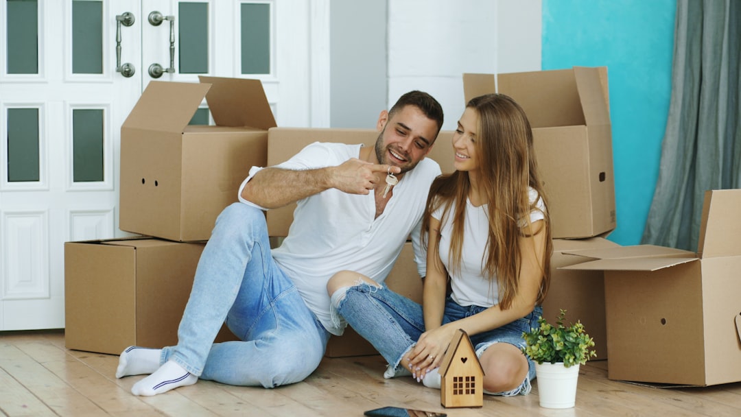 Services Happy couple sitting on floor in new house. Young man give keys to his girlfriend and kiss her